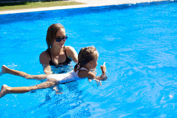 mom teaches her daughter to swim in the pool