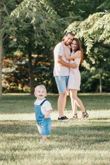 Fototapeta premium Happy smiling mother and father with baby boy in park outdoors. Family Caucasian mom and dad with son walking hugging in park on summer day. Happy family authentic lifestyle concept.