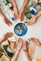 Conceptual flat lay with many hands and different waste, garbage types reaching planet Earth made...