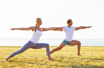 Fit man and beautiful woman practicing yoga outdoor on the grass. Stretching exercise in the sunset. Sport, fitness, health care and lifestyle concepts.