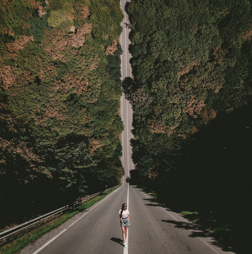 A young lady standing on a countryside asphalt road. Photo in the style of the film Inception. Dronewall.