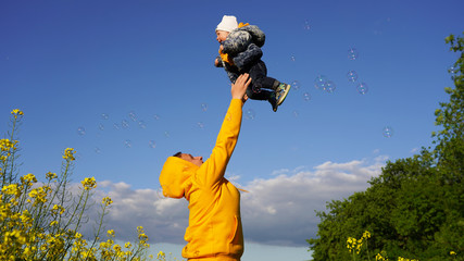 dad plays with a small child. father throws the baby into the air on a sunny day against the background of blue sky, yellow flowers and soap bubbles. carefree childhood, parental love, parenting