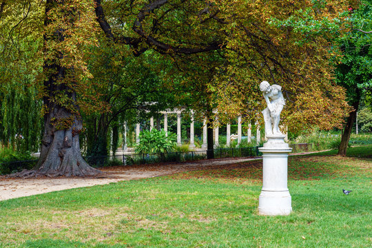 Statue Le joueur de billes (the marble player) in the Parc Monceau by Alfred Lenoir (1850-1920) with the famous classical roman colonnade in the background - Paris, France