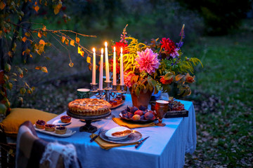 Autumn evening photo shoot - romantic dinner outdoors. Table with tablecloth and decoration - pie,...