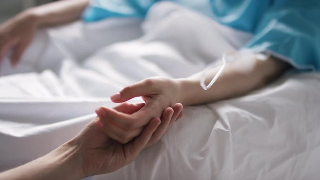 Handheld close up shot of unrecognizable man caressing hand of weak woman receiving treatment in hospital
