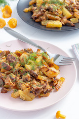 Fried forest chanterelle mushrooms with potatoes (Cantharellus cibarius). Two plates with delicious food on white wooden background. Vertical