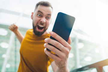 Guy being happy winning a bet in online sport gambling application on his mobile phone