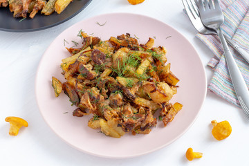 Fried forest chanterelle mushrooms with potatoes on a plate on white wooden background.