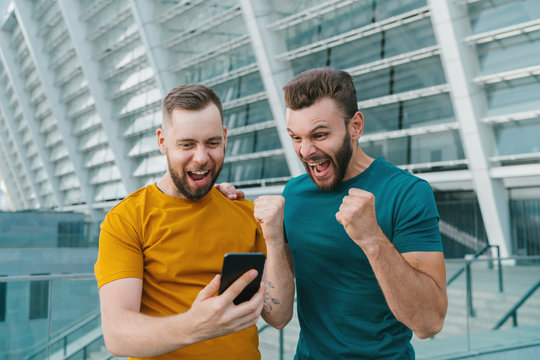 Men being happy winning a bet in online sport gambling application with football stadium on the background