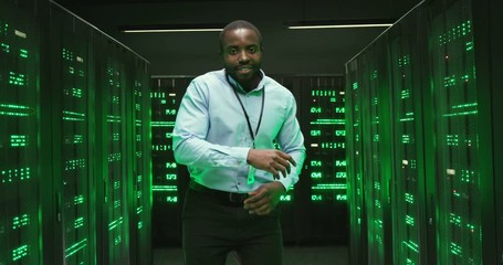 Cheerful happy African American young male technician or cryptograph dancing funny in big data storage center among processors. Joyful man analytic or technician dance and having fun among servers. - Powered by Adobe