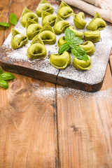 Tortellini e tortelloni typical dishes emilia italy. Food background with homemade raw Italian tortelloni and ingredients for green pesto on wooden background . High angle view. Copy space.