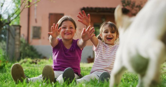 Authentic shot of two little girls are having fun together with their playful pedigreed puppy of Labrador Retriever dog outside a house in a sunny day. Concept: love for animals, childhood, friendship