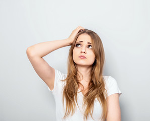 Fototapeta premium Thinking blond doubt young woman looking up and thinking on light blue background. Closeup portrait