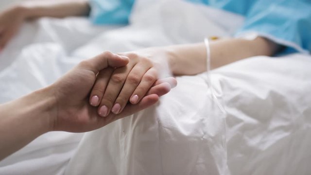 Close up shot of unrecognizable man holding hand of sick woman lying in hospital bed