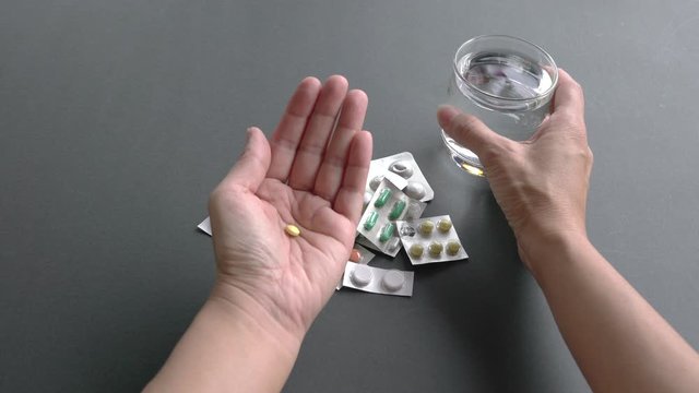 Adult woman taking medical pill with a glass of water. Close up view of her hands. Illness or sick health concept. 