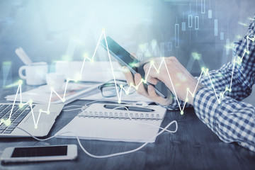 Double exposure of man's hands holding and using a digital device and forex graph drawing. Financial market concept.