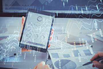 Double exposure of man's hands holding and using a digital device and forex graph drawing. Financial market concept.