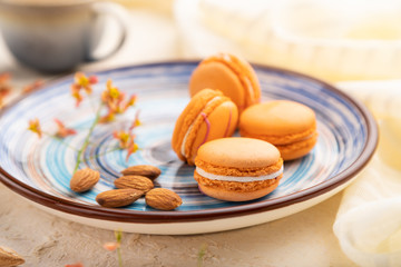 Orange macarons or macaroons cakes with cup of coffee on a white concrete background. Side view, selective focus.