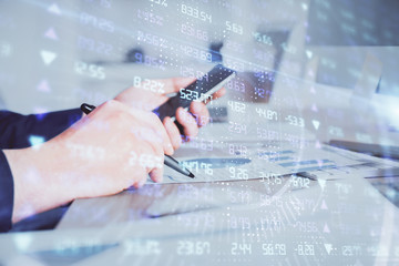 Double exposure of man's hands holding and using a phone and financial graph drawing. Analysis concept.