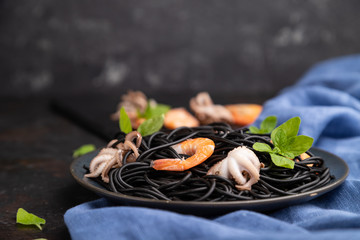 Black cuttlefish ink pasta with shrimps or prawns and small octopuses on gray wooden background. Side view, selective focus.