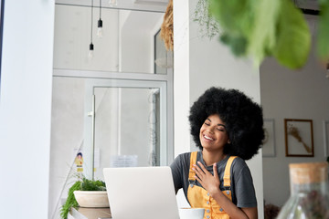 Happy hipster African American teen girl student with Afro hair using laptop computer laughing...