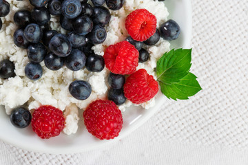 natural cottage cheese with raspberries and blueberries on a white plate, with mint leaves, on the background of a textile linen napkin