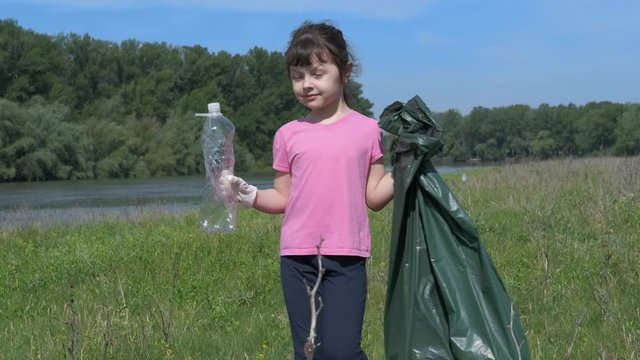 Child takes care of field. Little girl collects plastic bottles scattered in the meadow in the trash.