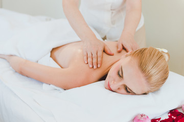 Beautiful woman lying on the bed for a spa asia massage at luxury spa and relaxation. The masseuse is massaging her back and shoulders in the spa room.