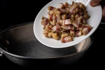 Preparing Spaghetti Carbonara on a black stove with pork guanciale on a white plate on an aluminum pan
