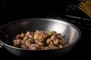 Preparing Spaghetti Carbonara on a black stove with pork guanciale in an aluminum pan