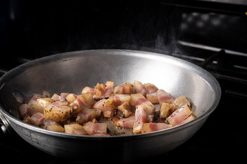 Preparing Spaghetti Carbonara on a black stove with pork guanciale in an aluminum pan