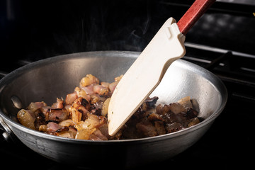 Preparing Spaghetti Carbonara on a black stove with pork guanciale in an aluminum pan