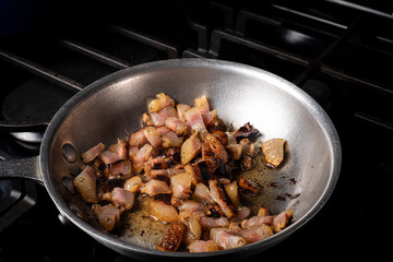 Preparing Spaghetti Carbonara on a black stove with pork guanciale in an aluminum pan