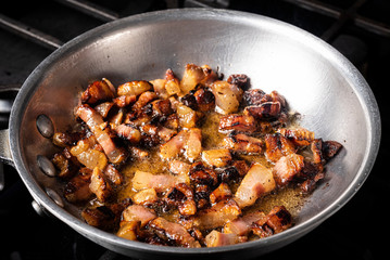 Preparing Spaghetti Carbonara on a black stove with pork guanciale in an aluminum pan