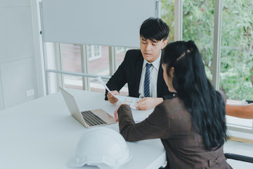 Asian male and female colleagues are discussing  work with graph paper and a notebook.
