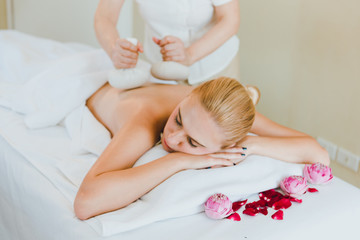 Beautiful woman lying on the bed for a spa asia massage at luxury spa and relaxation. The masseuse is massaging her back using a cloth massage device in the spa room.