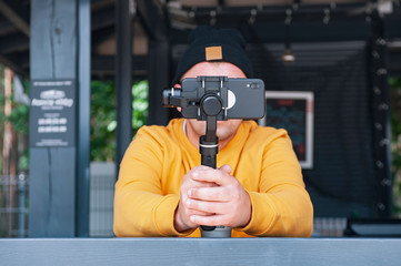 Blogger in coffee shoots video on a smartphone with a manual camera stabilizer.