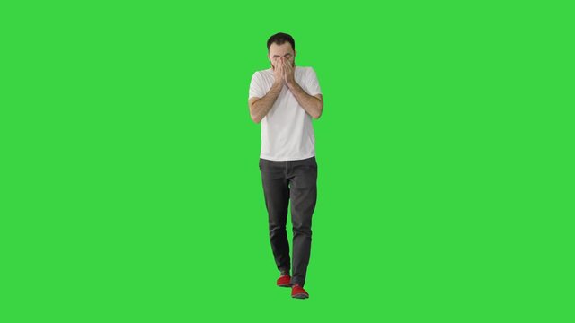 Sleepy male in white t-shirt yawning and rubbing eyes while walking on a Green Screen, Chroma Key.