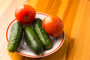 Fresh Tomatoes and Cucumbers on Plate Against Wooden Table.
