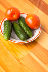 Fresh Tomatoes and Cucumbers on Plate Against Wooden Table.