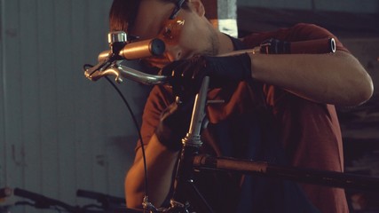 theme small business bike repair. A young Caucasian brunette man wearing safety goggles, gloves and apron uses hand tool to repair and adjust the Handbrabar brake bike handle in garage of workshop