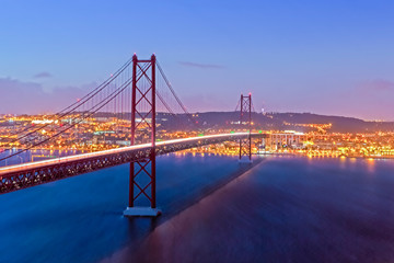 Portugal Travel Destinations. Crossing The Tagus River. Amazing Image of Lisbon Cityscape Along with 25th April Bridge (Ponte 25 de Abril). Taken from Almada District. Picture Taken at Twilight.