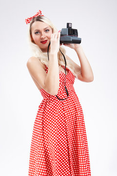 Pin-up Girl Ideas. Portrait of Sensual Caucasian Blond Girl Posing in Pin-up Style. Holding Instant Camera in Front. Against White.