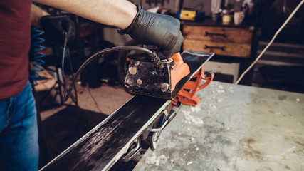 Applying hot wax to ski base with iron. Applying Ski Wax To Ski Base. Ski base tuning. Ski wax iron and wax bars. Ski service and repair. repairman in workshop ski service. Man Waxing Ski In Workshop
