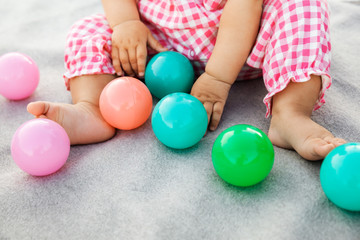 Infant baby girl sitting on a gray blanket and playing with colorful plastic balls