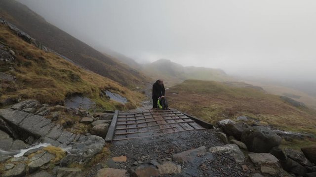 Pan left to right of water flowing down Snowdon mountain revealing Man hiker packing up backpack on Pyg Track Wales Snowdonia