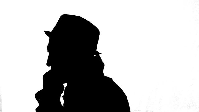 Mysterious man in coat and hat turning around, black silhouette on white background.