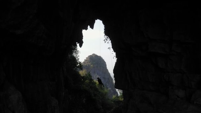 Amazing rock climber abseiling cave, aerial pull-back reveal of natural archway
