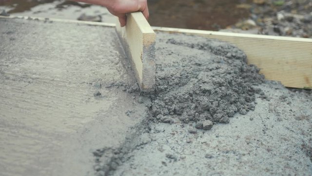 Tapping flattening fresh cement with wooden board