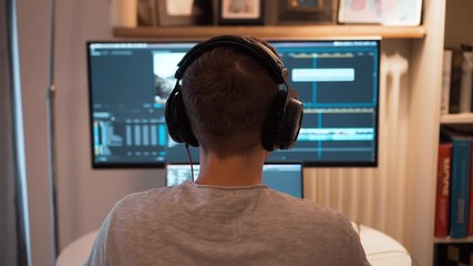 View from behind of a young video editor putting his headphones on before start working